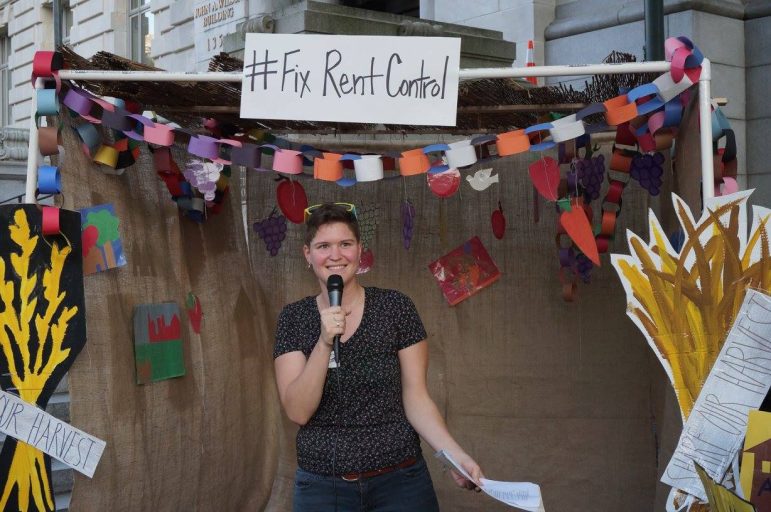 Person in a Sukkah talking with a microphone, the Sukkot has a sign that reads #FixRentControl