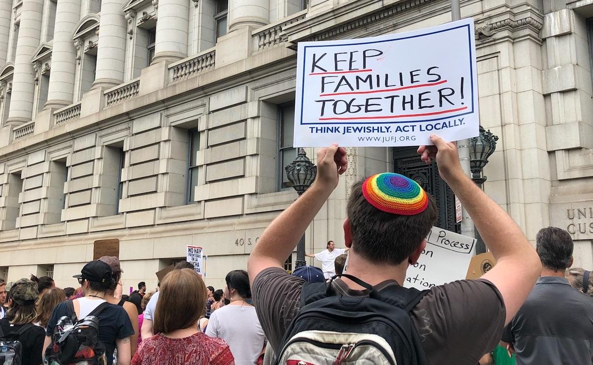 a crowd of protestors; one person is holding a JUFJ sign that reads: keep families together!