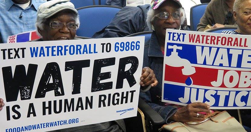 two people holding signs at a water rally