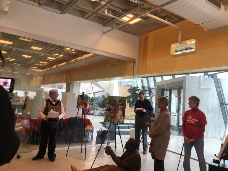 Kimberly Sheridan delivers remarks at University of Baltimore library beside her paintings