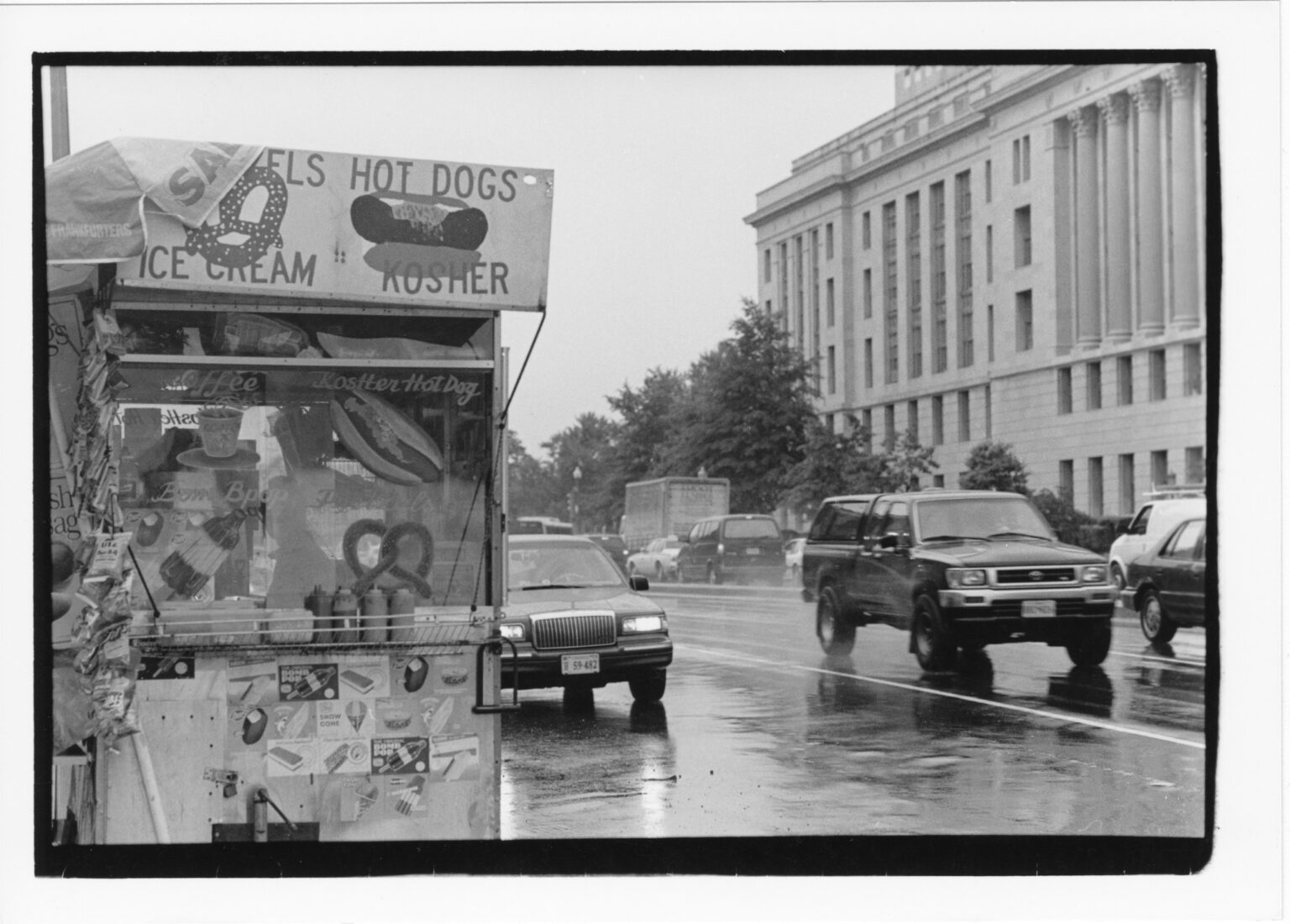 A street vendor advertising kosher hot dogs along 14th Street NW near the U.S. Holocaust Memorial Museum in downtown DC. Department of Agriculture building visible across the street, 1998. Photograph by Lloyd Wolf. Lillian and Albert Small Capital Jewish Museum Collection. Gift of the photographer.